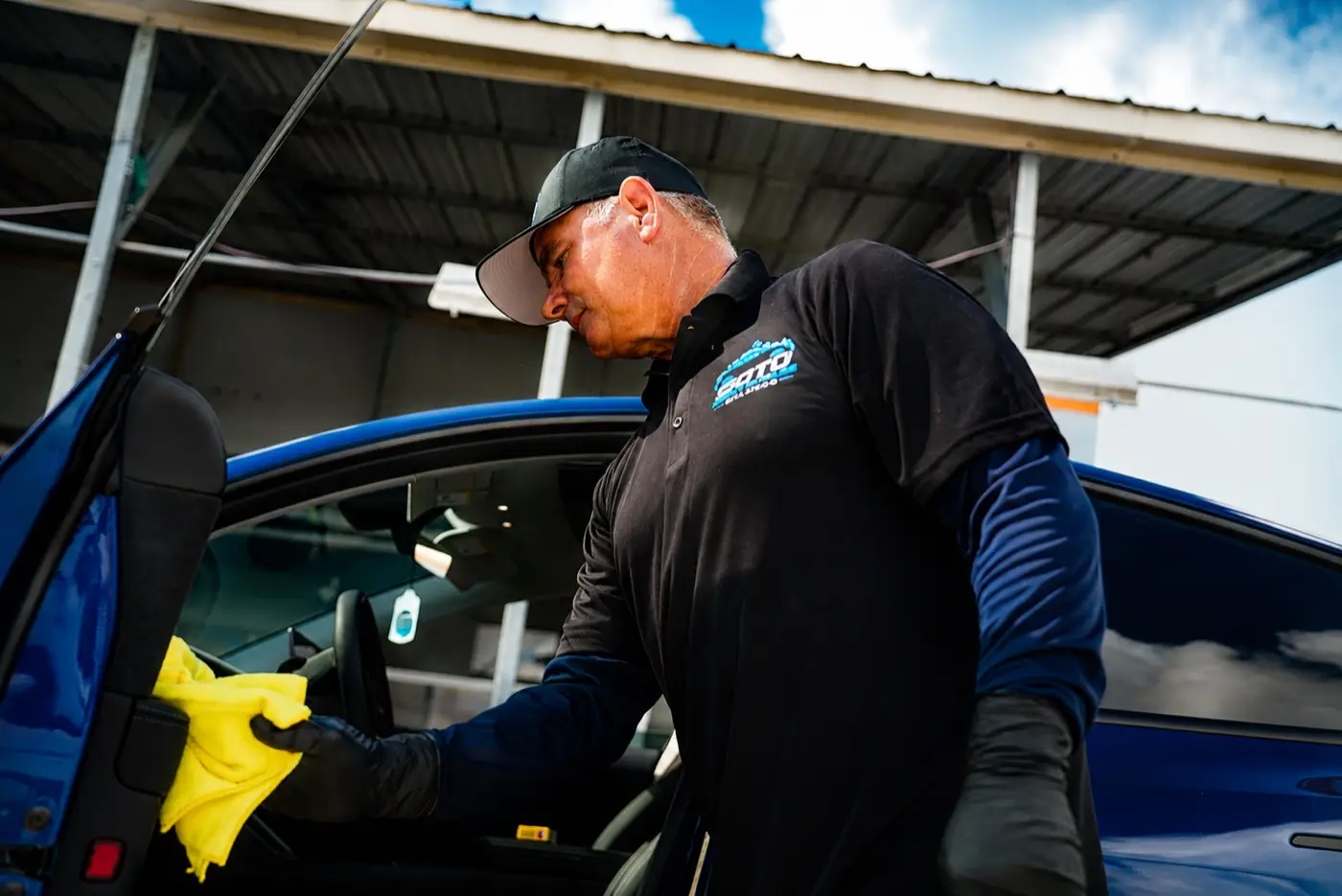 Soto detailer wiping down a blue car's door jamb with a microfiber towel under the mobile canopy